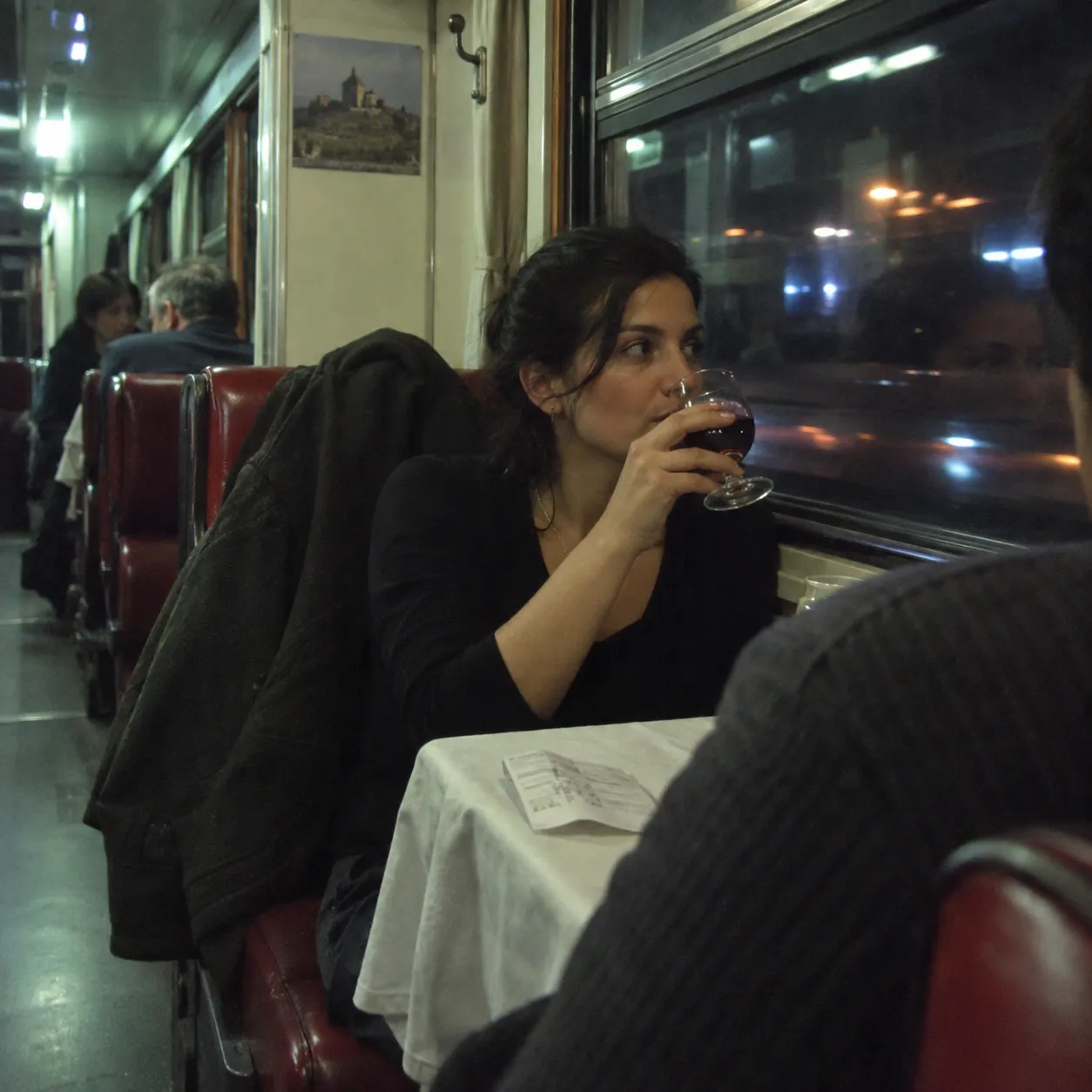 アレクサンドロウリの赤ワインをグラスで、夜行列車の食堂車の窓辺で。壁に山上の教会の写真(イメージ)