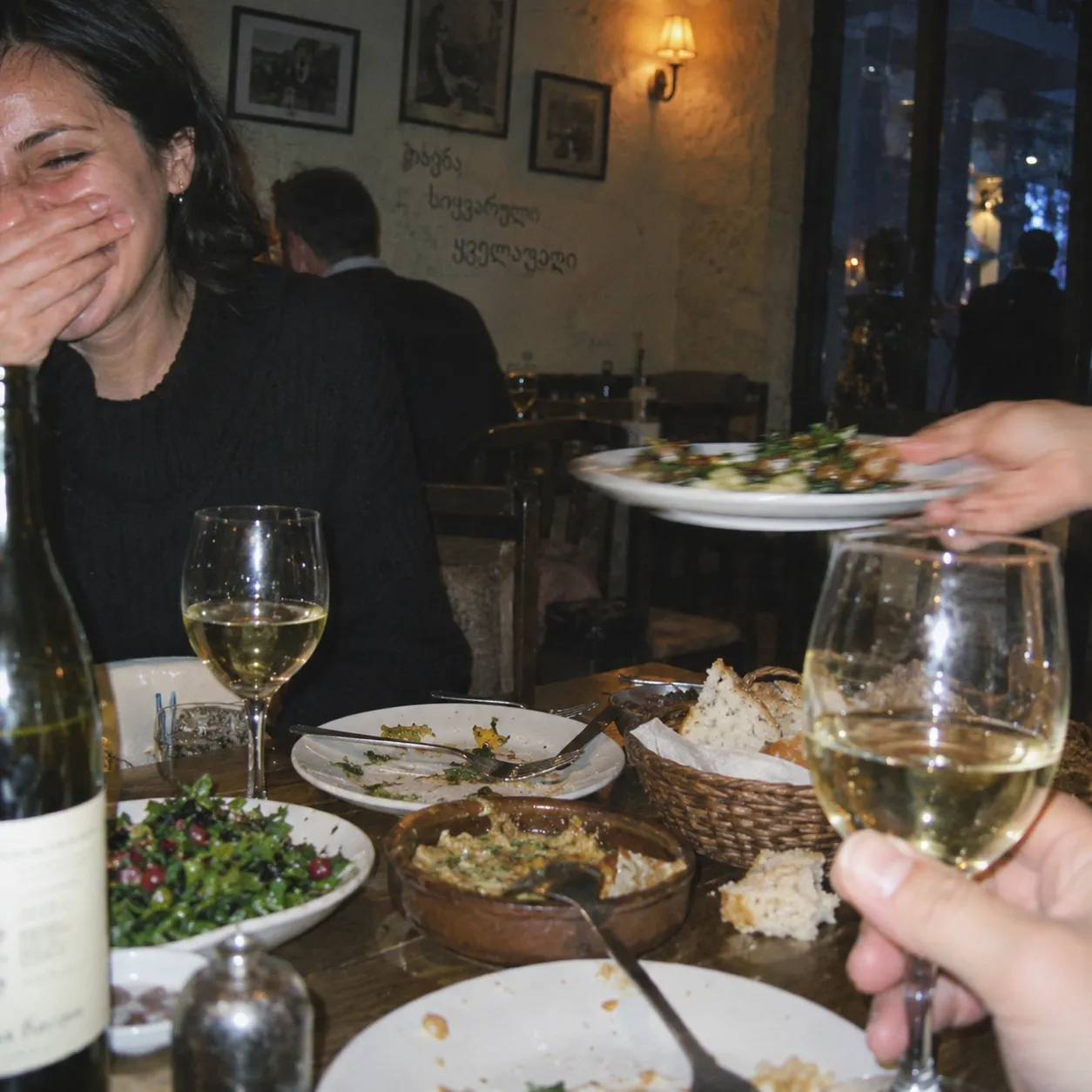 チヌリの白ワインをグラスに、トビリシのレストランで前菜とパンを囲む夜の食卓(イメージ)