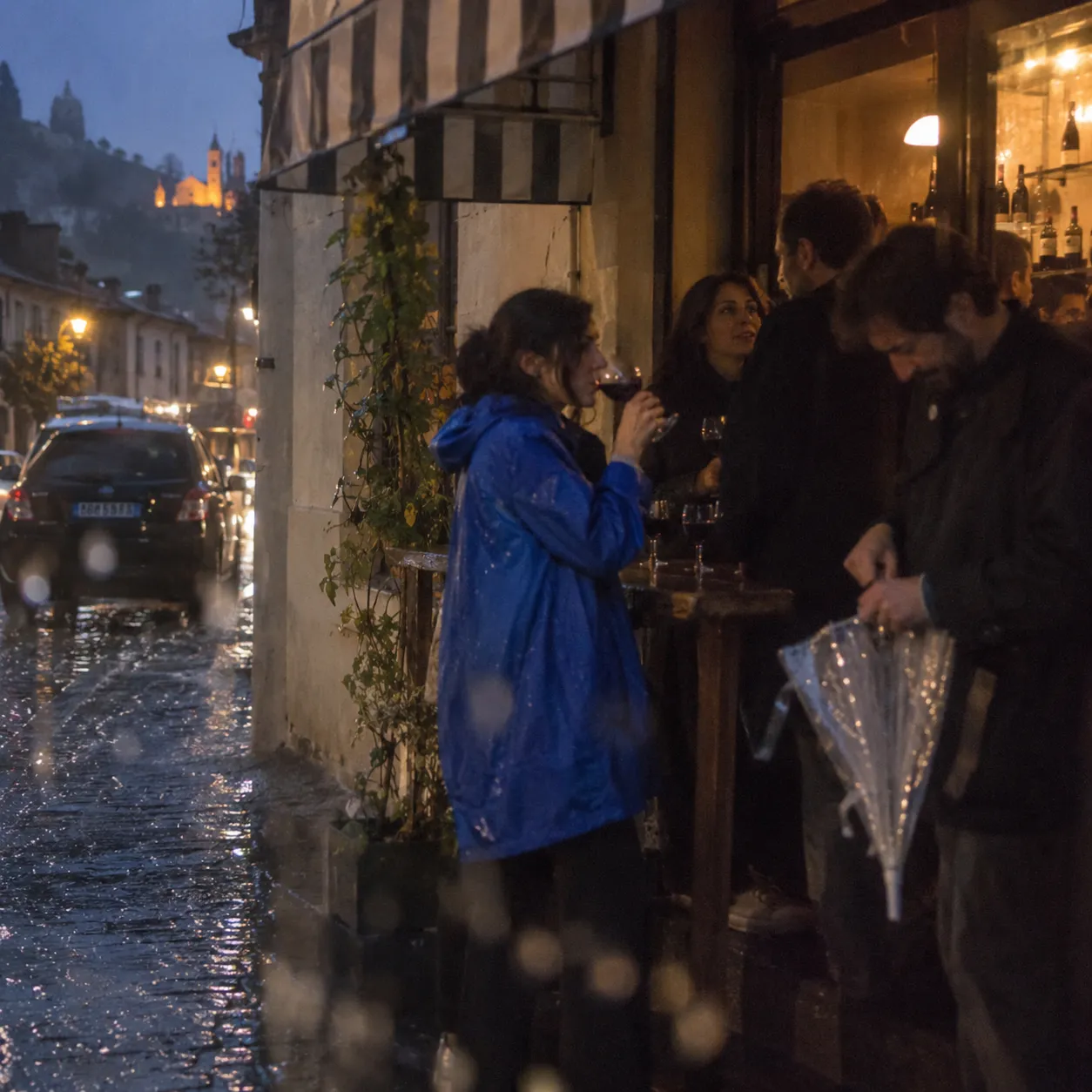 オツハヌリ・サペレの赤ワインをグラスに、雨の夕暮れ、石畳の通りに面したワインバーの軒先で(イメージ)