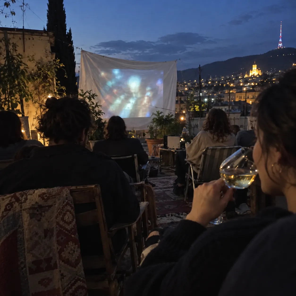 ツィツカの白ワインをグラスに、トビリシの屋上で夜の野外上映を眺めながら。丘の上の灯りとテレビ塔(イメージ)