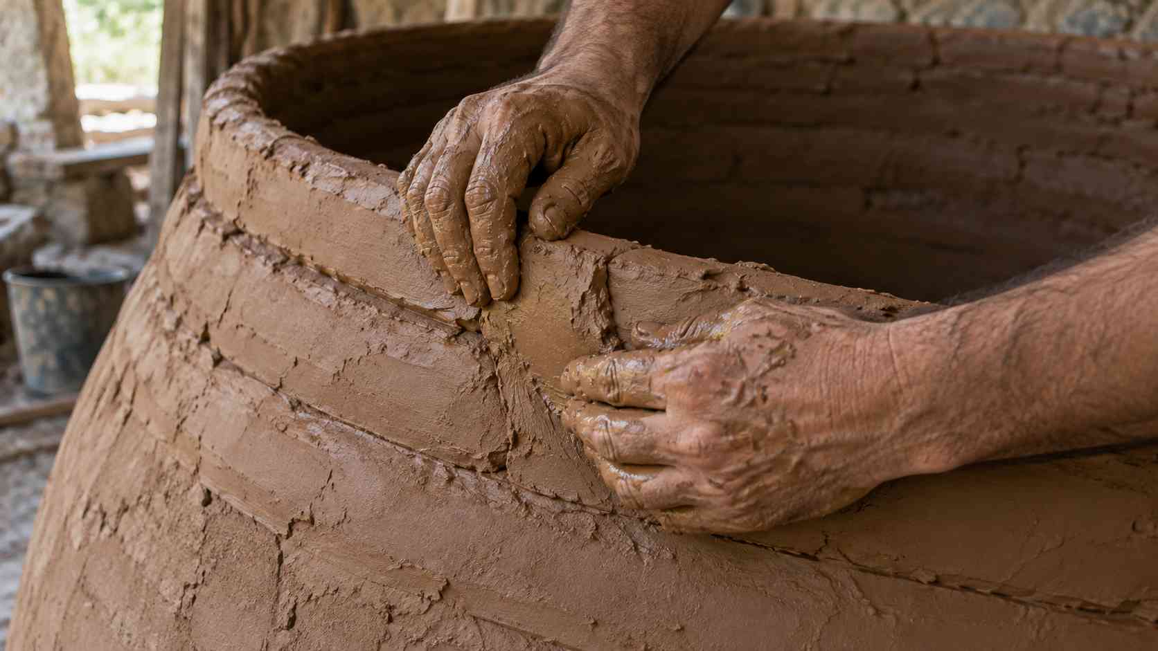 粘土を積み上げて、クヴェヴリの壁を形づくる職人の手(イメージ)